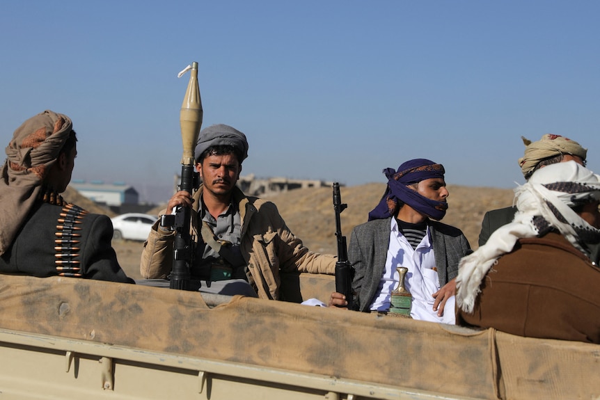 Four Houthis holding up rifles and wearing scarves around their heads.