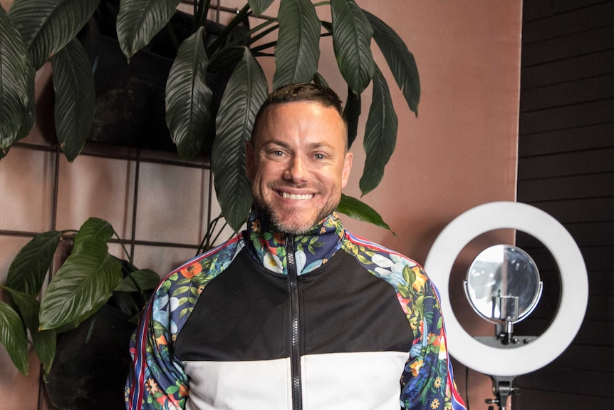 A man smiling and wearing a multi-coloured top for a story about the dos and don'ts of colouring hair at home.