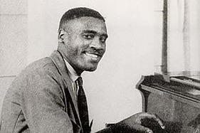 Monochrome of man smiling at a piano.