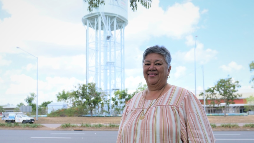 A woman standing on a roadside with a water tower behind.