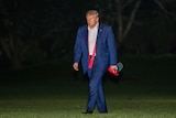 Donald Trump looking sad while walking across a lawn at night with his tie untied and a MAGA hat in his hand