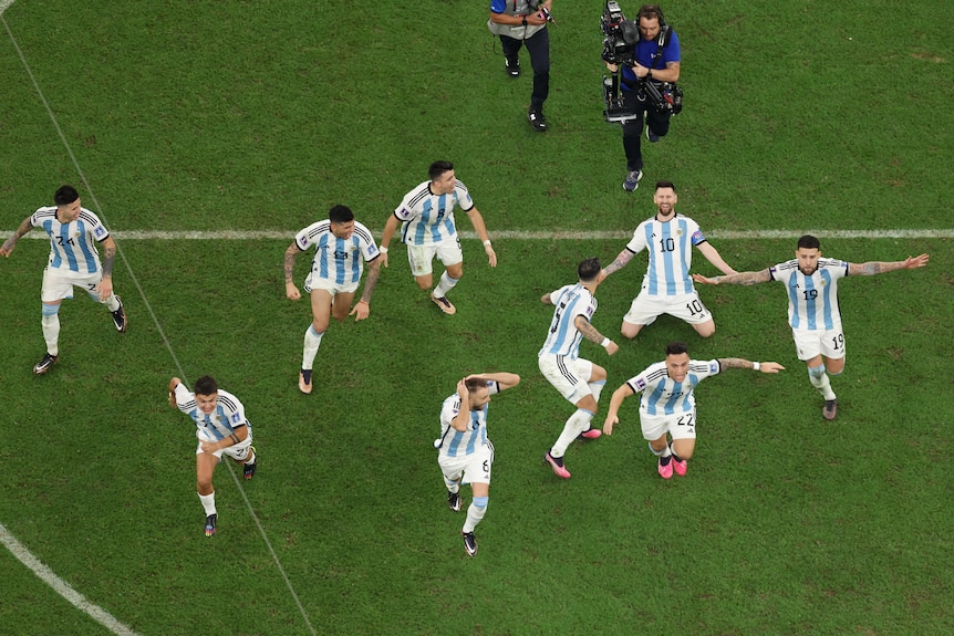 Lionel Messi is on his knees as Argentina players run forward to celebrate winning the FIFA World Cup final.