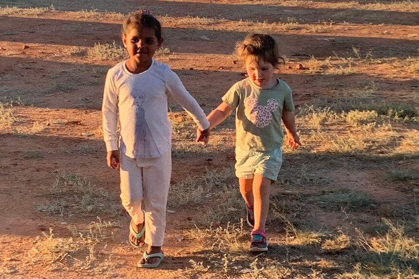 Two young girls holding hands while they go for a walk.