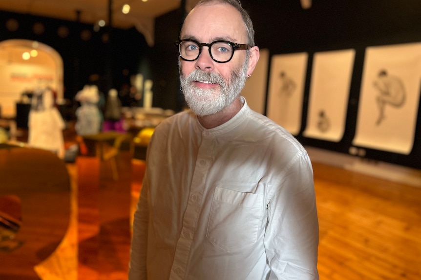 A man with black horn rimmed glasses stands in a gallery