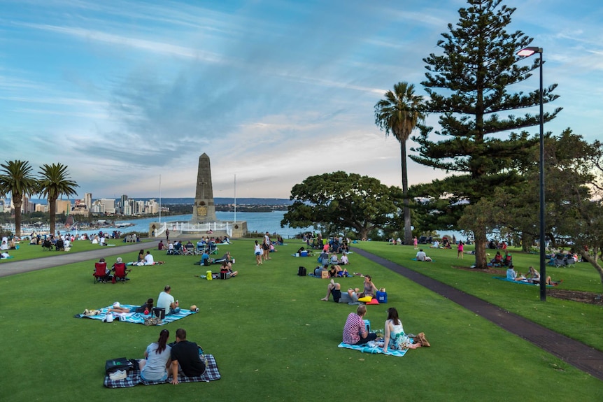 Late afternoon view over the city, people picnicking on lush green grass of Kings Park and the war memorial in the foreground.