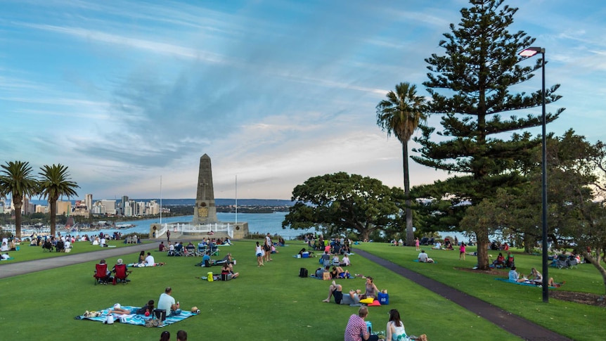 Late afternoon view over the city, people picnicking on lush green grass of Kings Park and the war memorial in the foreground.