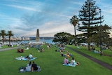 Late afternoon view over the city, people picnicking on lush green grass of Kings Park and the war memorial in the foreground.