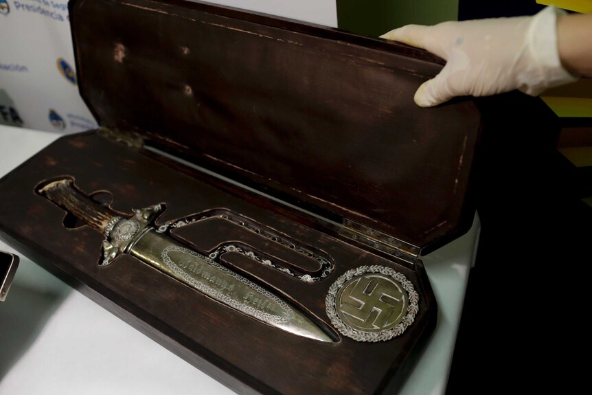 A knife with Nazi markings in a wooden case next to a golden swastika.