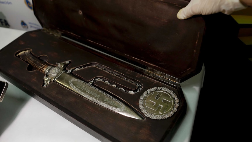 A knife with Nazi markings in a wooden case next to a golden swastika.
