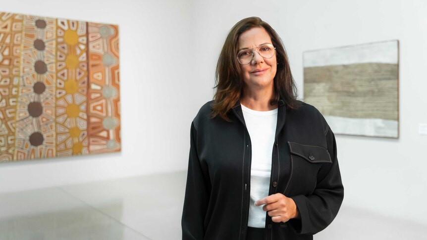 Hetti Perkins pictured in front of two pieces of Indigenous artwork.