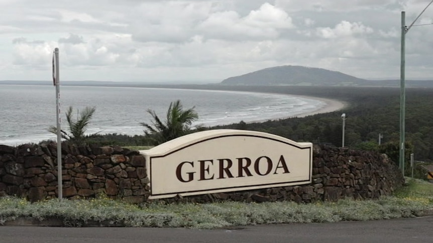 A brick wall on top of a hill overlooking Gerroa beach on a cloudy day. There are large letters spelling out GERROA on the sign.