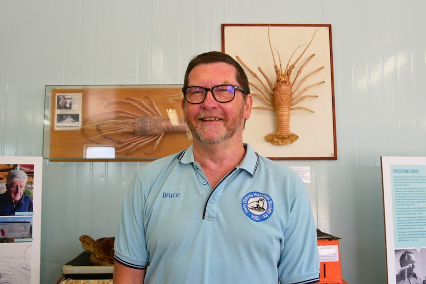 A man in a blue shirt stands in front of two framed lobsters