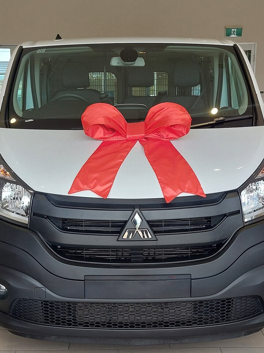 A brand new Mitsubishi van with a big red ribbon on the bonnet.