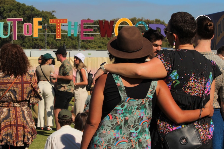 Two women stand with their arms around each other at a music festival.