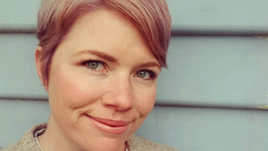 Clementine Ford, with pink hair, poses against a wooden building.