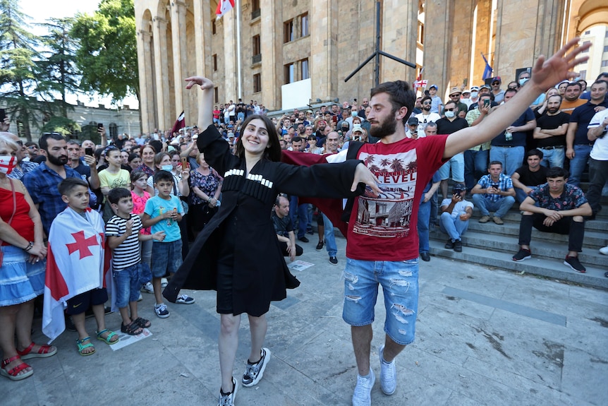 A man and woman dance ringed by people outside of a building.