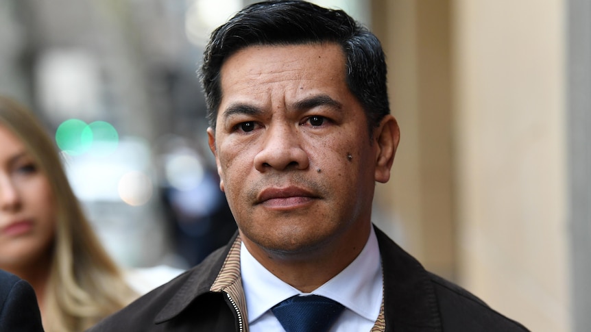 A man with dark hair looks serious as he is photographed outside court.