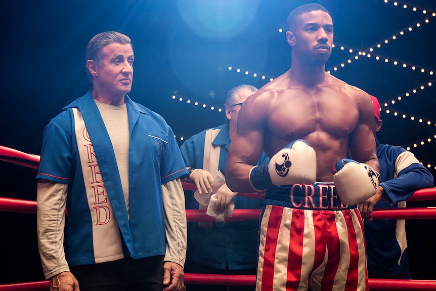 Colour photo of Michael B Jordan and Sylvester Stallone standing in boxing ring in 2018 film Creed II.