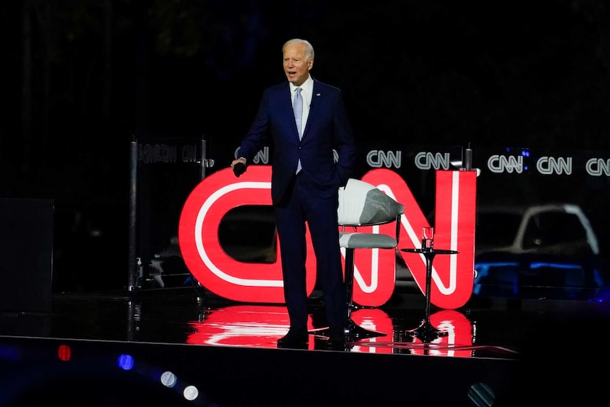 Joe Biden in a suit in front of a CNN logo on stage looks out at the audience with his mouth open.
