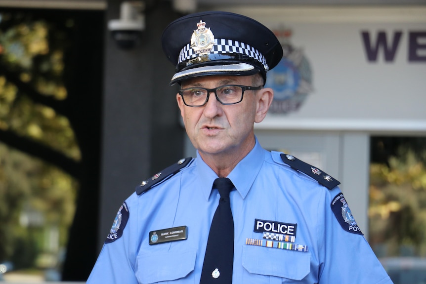 A man in a police uniform looks slightly to the left of frame wearing glasses as he speaks.