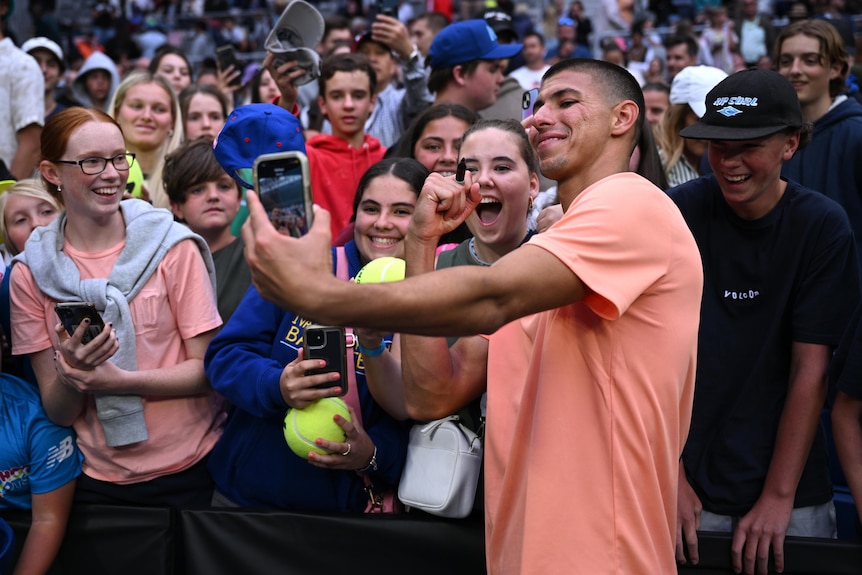 An Australian male tennis player poses for a selfie with spectators at the Australian Open.