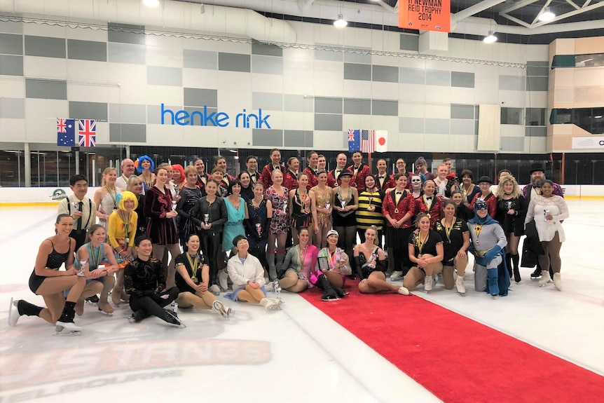 A group of figure skaters in various costumes posing for a group photo on the ice.