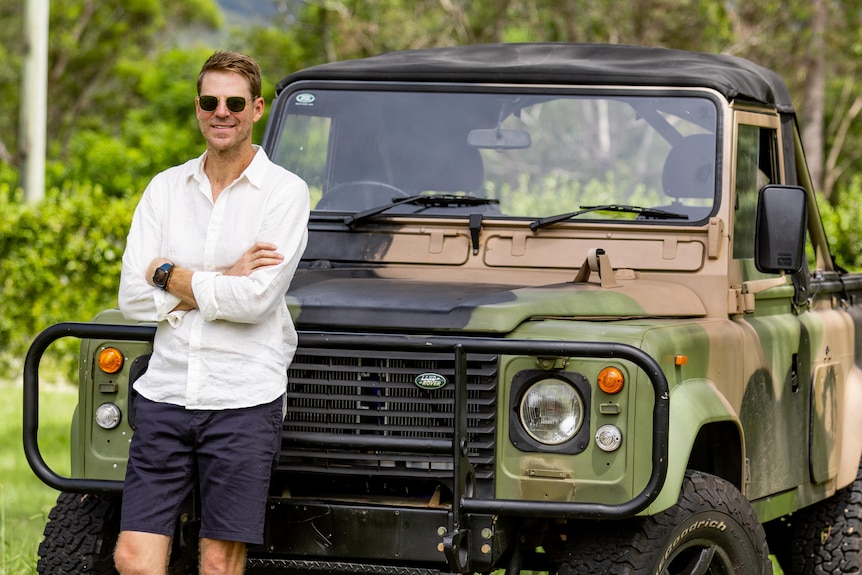 A man leans against the ute which is painted in camouflage colours.