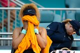 Naomi Osaka holds her head in an orange towel at the Miami Open