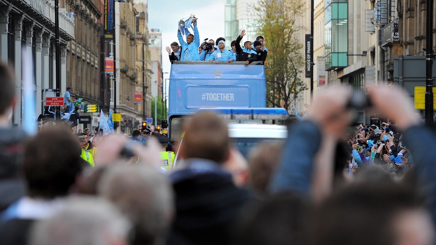 Manchester City players celebrate Premier League title on bus heading through Manchester.