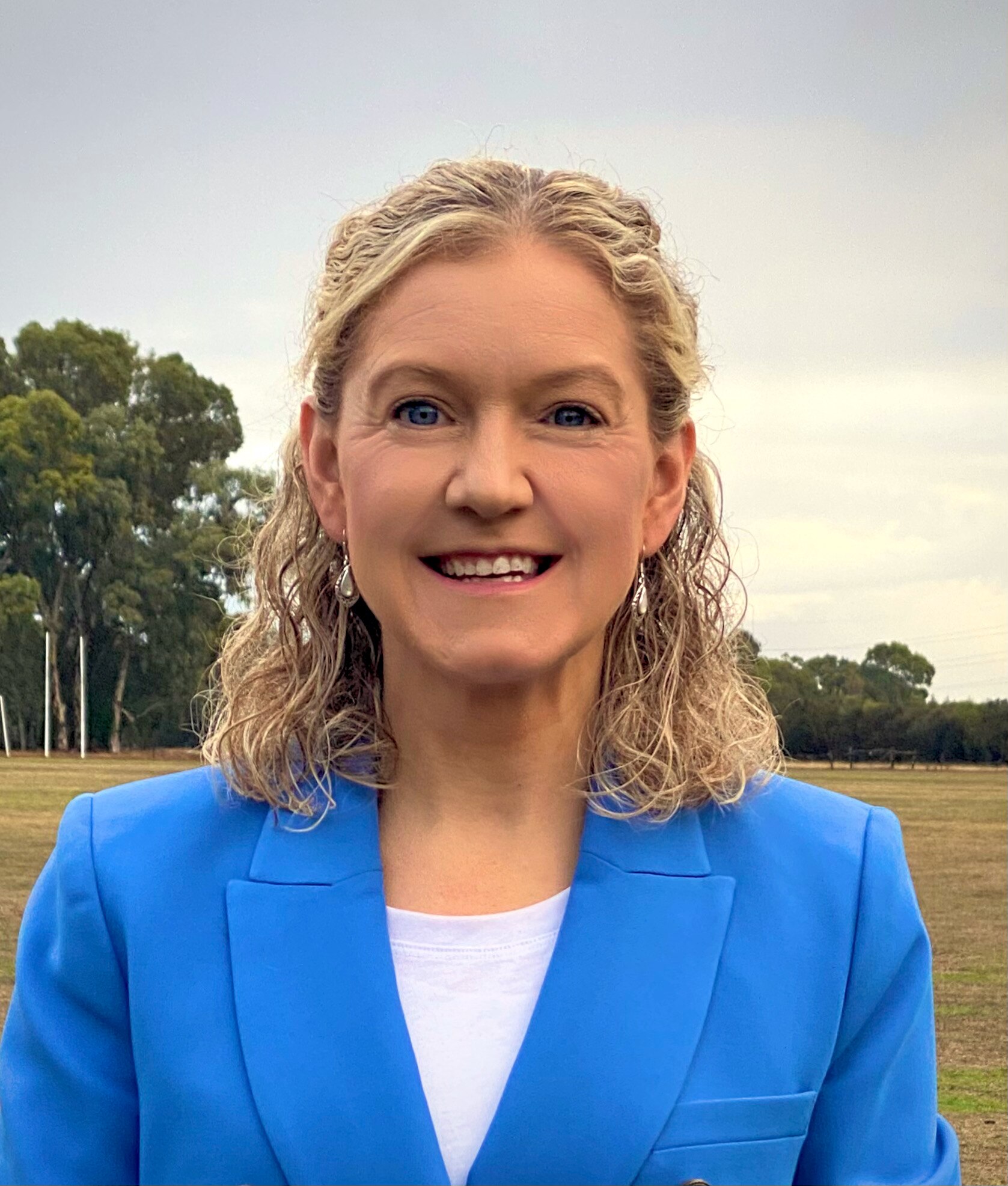 A woman stands in a park and smiles at the camera