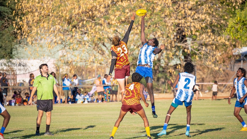 A Halls Creek Hawks and Kururrungku Roos player hit out in the ruck. 