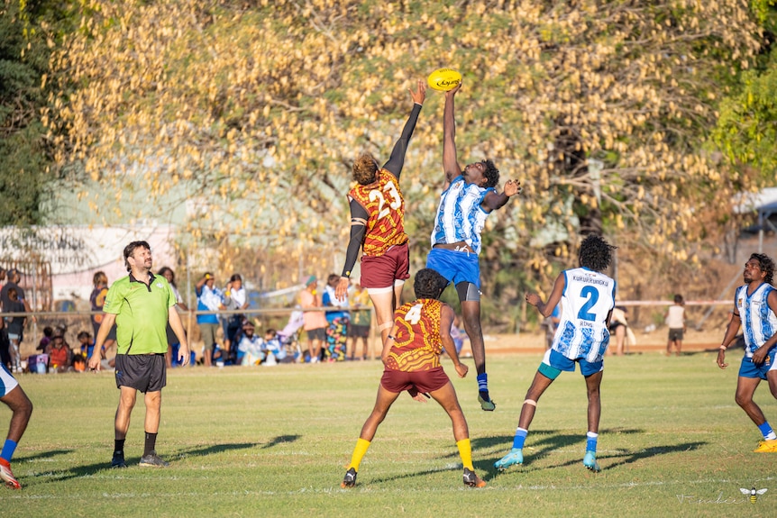 A Halls Creek Hawks and Kururrungku Roos player hit out in the ruck. 