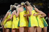Netball players wearing green and gold jerseys huddling together.