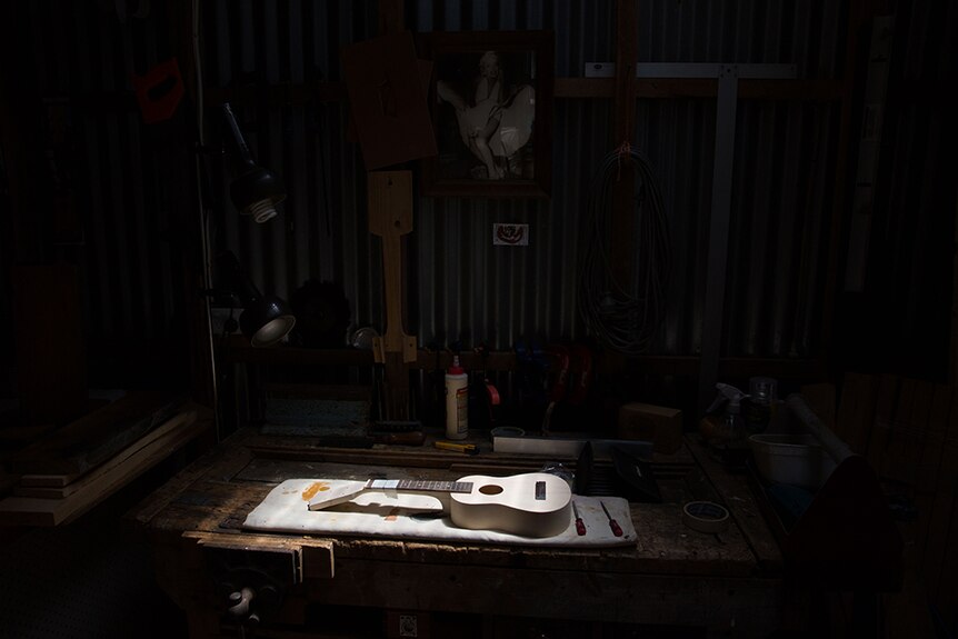 Ukulele on a workbench under spotlight.