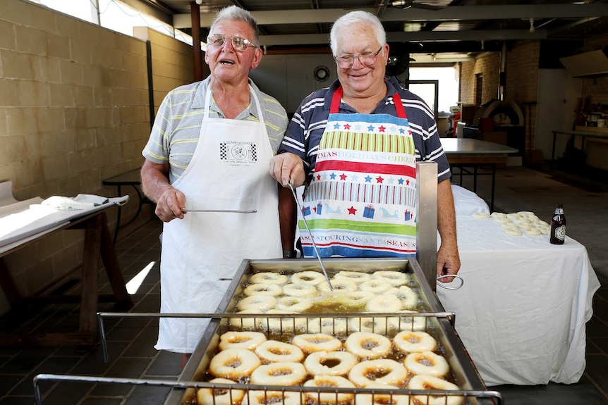 Two men stand by a deep fryer as they cook Grispelle, Italian doughnuts, together.