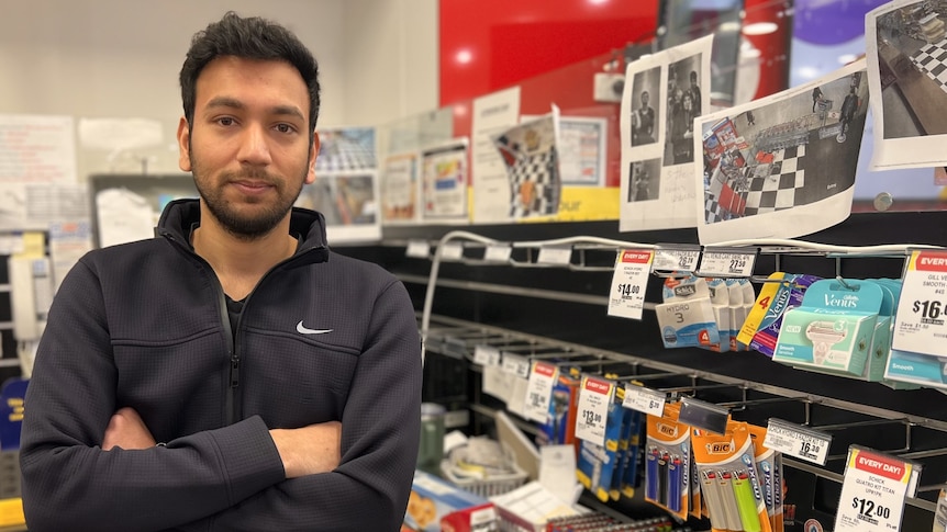 A man with black hair olive skin stands arms folded near security camera photos of shoplifters