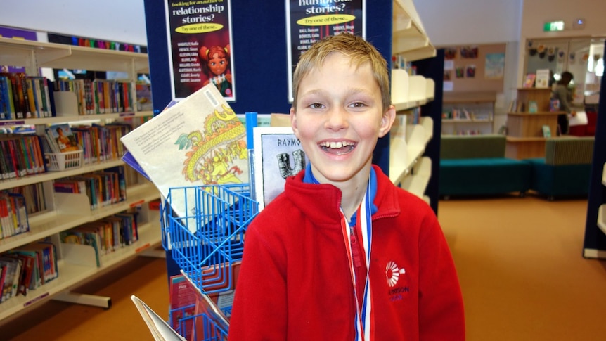 Angus Crockett smiles — standing in his school library.