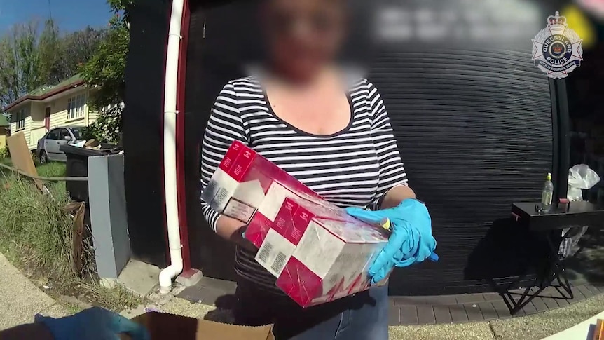 Woman holding siezed cigarette cartons. 