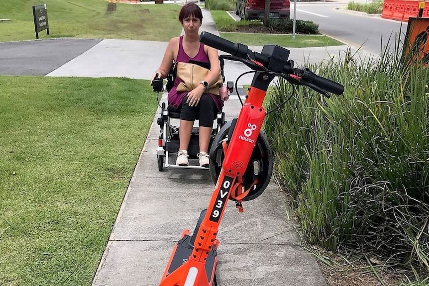 An e-scooter blocking the path of a woman in a wheelchair a pedestrian footpath in Brisbane.