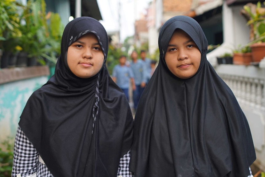 12-year-old twins Athyyah Alya and Athyyah Kamila Aziza, wearing headscarves and identical black and white chequered dresses.