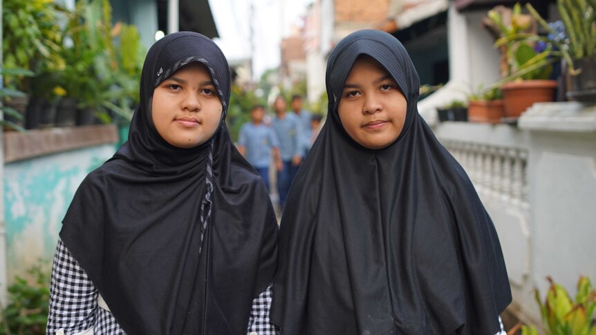 12-year-old twins Athyyah Alya and Athyyah Kamila Aziza, wearing headscarves and identical black and white chequered dresses.