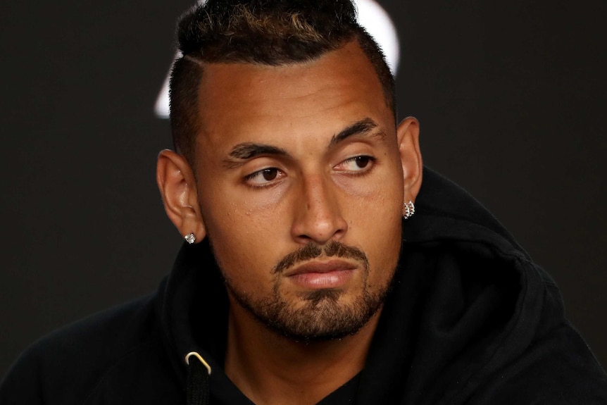 A tight shot of Nick Kyrgios, wearing a black shirt, looking to his left during a press conference.