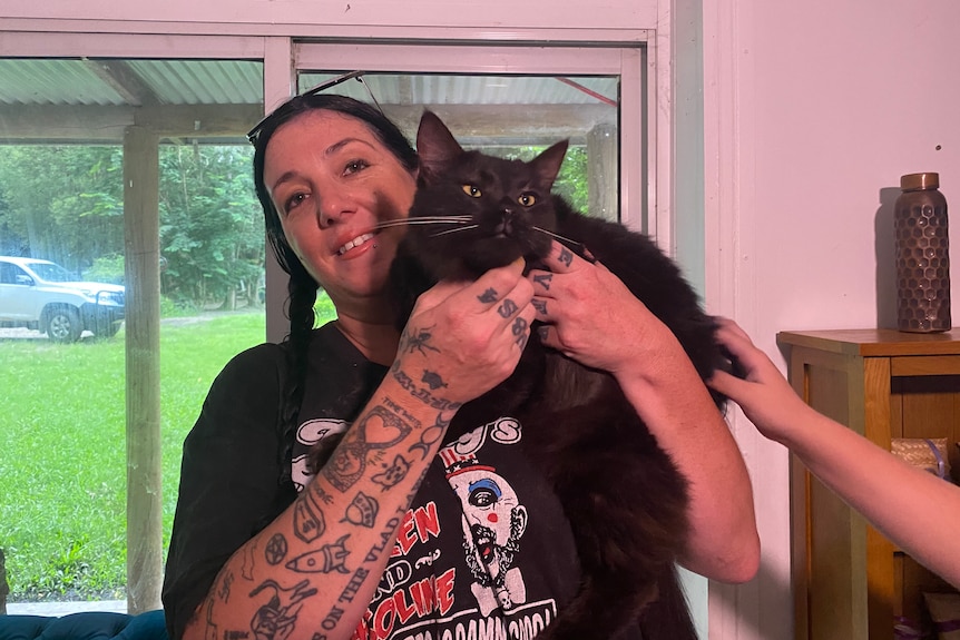 woman with black hair holds black cat towards camera