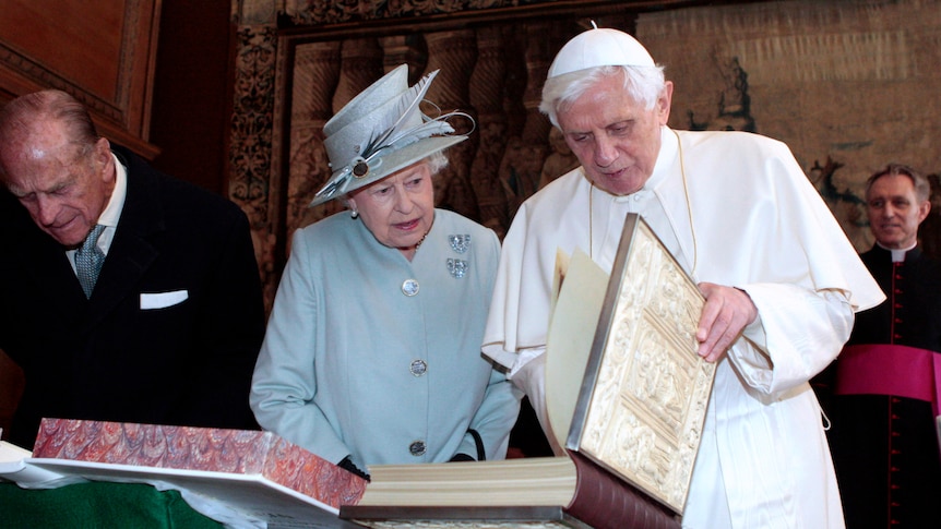 queen elizabeth II and pope benedict XVI looking down at large embellished book