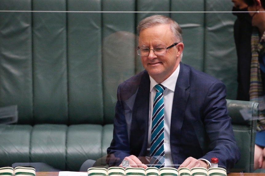 A man in a suit behind a glass partition inside the House of Representatives chamber.