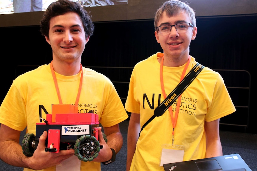 Two university students stand holding their robot car