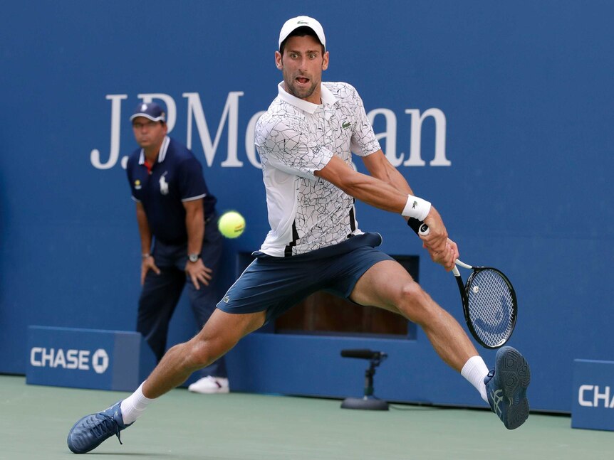 A male tennis player prepares to hit a two handed backhand shot on the run with his legs wide apart