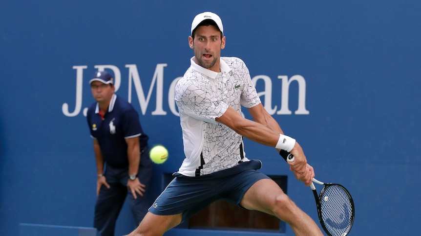 A male tennis player prepares to hit a two handed backhand shot on the run with his legs wide apart