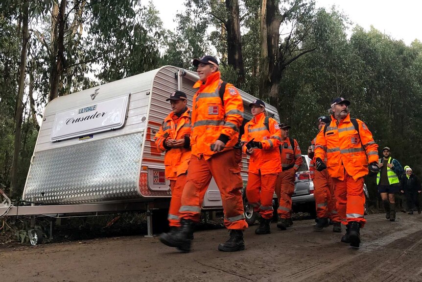 SES volunteers wearing orange high-vis jackets and pants walk as a group on a path in a state forest.