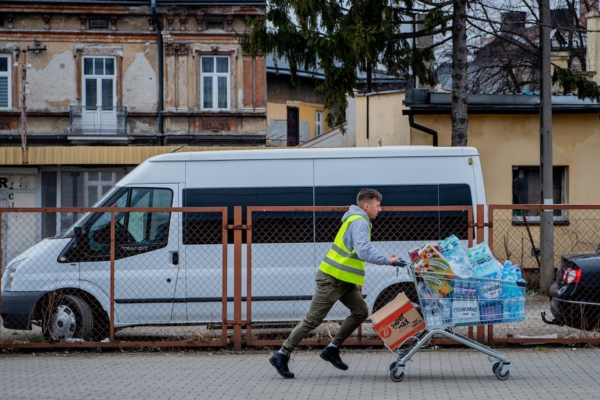 A man in a high vis vest pushes a trolley filled with water bottles 